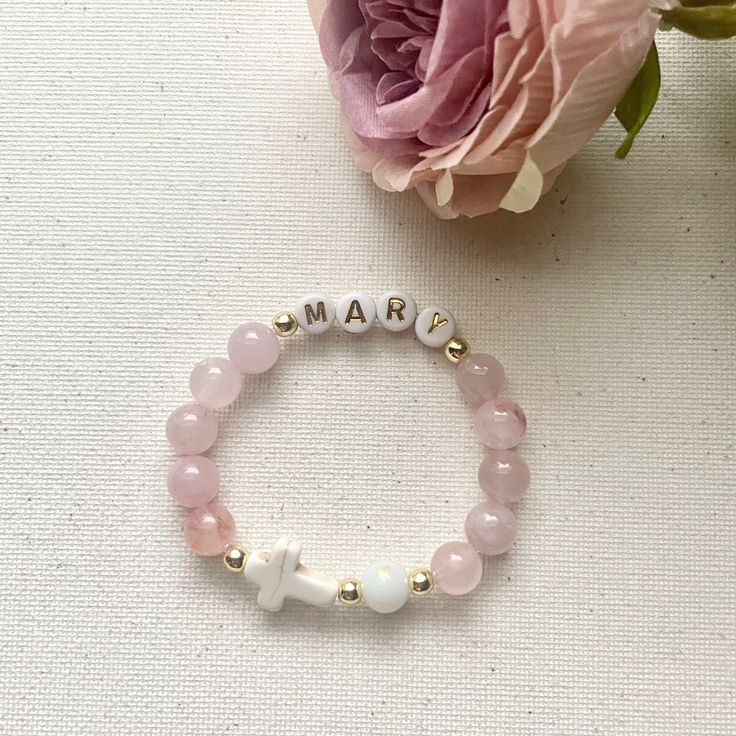 a bracelet with the word mar written on it and a pink flower next to it