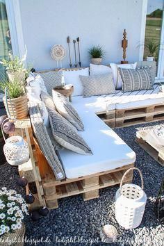 a couch made out of wooden pallets sitting on top of a gravel covered ground