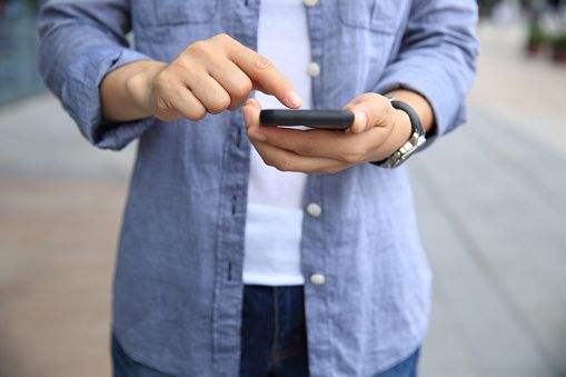 a person holding a cell phone in their hand while standing on the street with other people