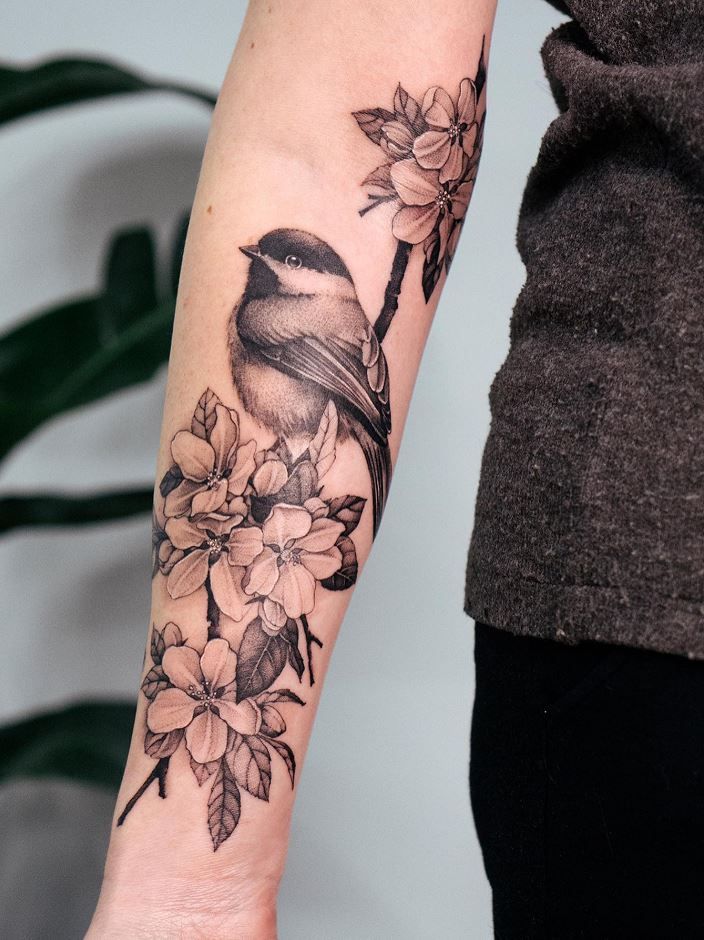 a small bird sitting on top of a branch with flowers around it's arm