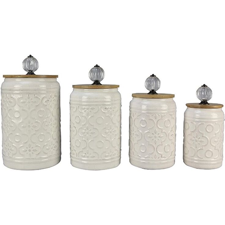 three white canisters with lids and knobs on each one is decorated with an intricate design