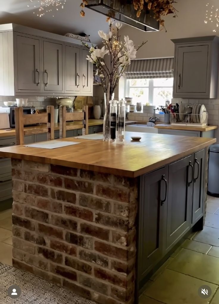 a kitchen with an island made out of bricks and wooden counter tops, surrounded by gray cabinets