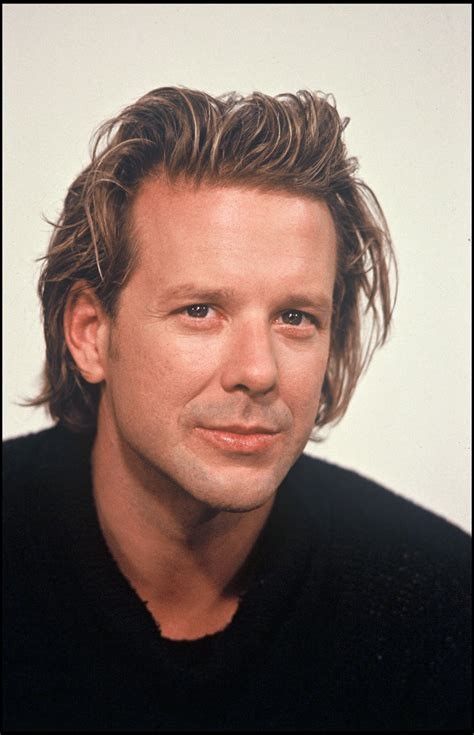 a close up of a person wearing a black shirt and posing for a photo with his hair blowing in the wind