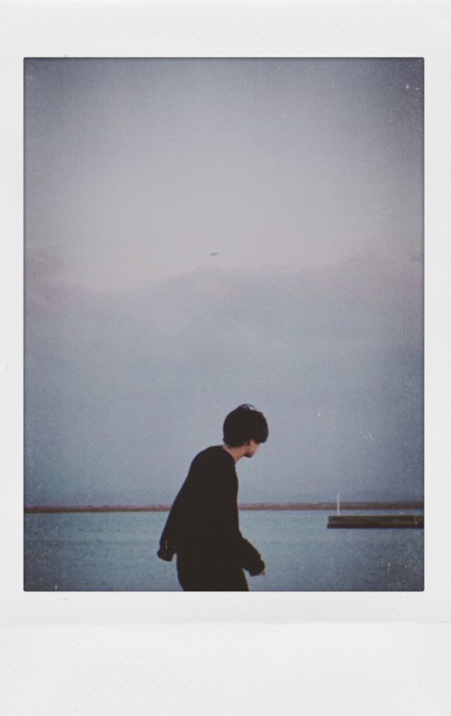 a polaroid photograph of a man walking by the water