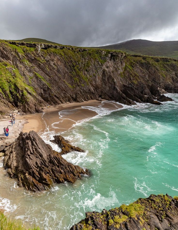 people are walking along the beach by the water's edge on a cloudy day