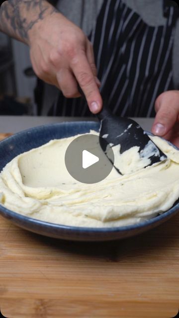 a person is spreading cream on top of some food in a blue bowl with a black and white spatula