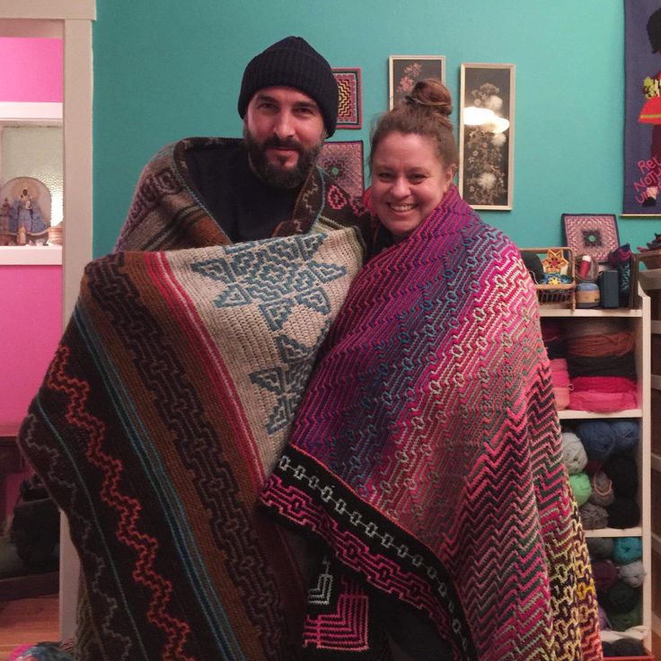 a man and woman holding a blanket in their living room with pictures on the wall behind them