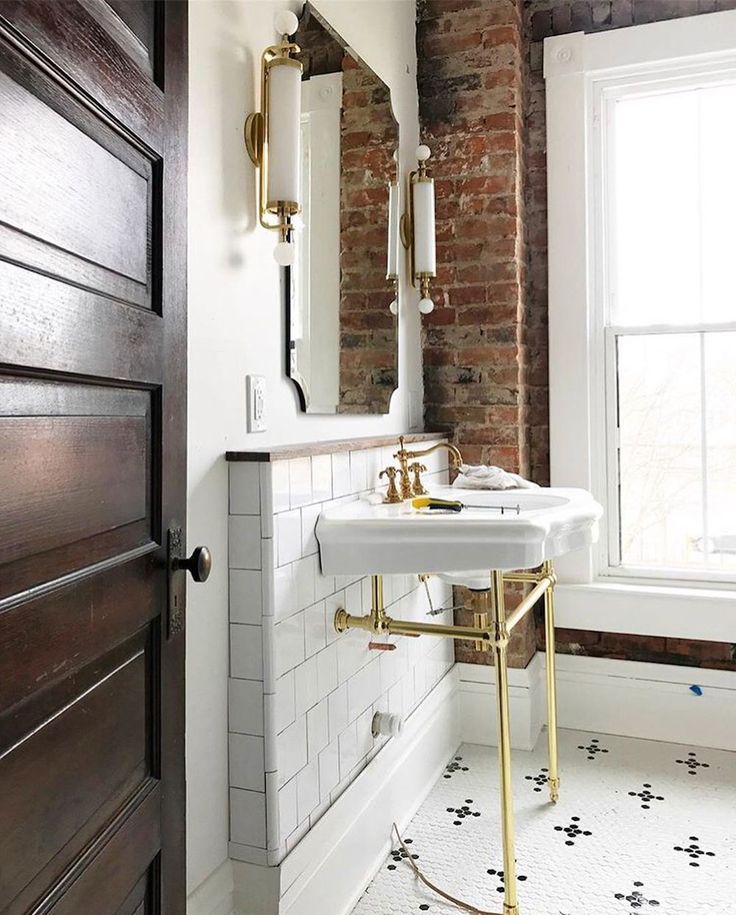 a bathroom with brick walls and white tile flooring, gold fixtures and an antique style sink