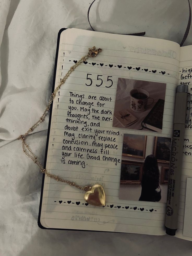 an open notebook with writing on it and a gold heart charm hanging from the pages