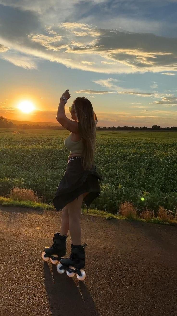 a woman riding a skateboard on top of a dirt road near a lush green field