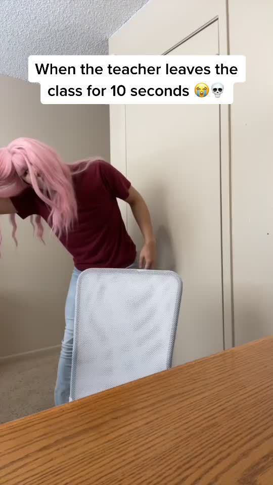 a woman with pink hair leaning on a chair and texting, when the teacher leaves the class for 10 seconds