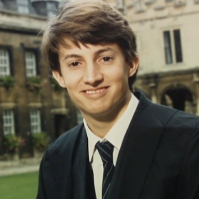 a man wearing a suit and tie in front of a building with an ivy covered courtyard