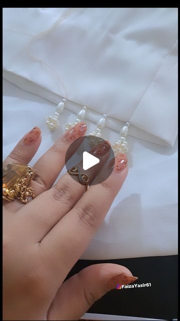 a woman's hand with gold and brown nail polish on her nails, next to a beaded necklace