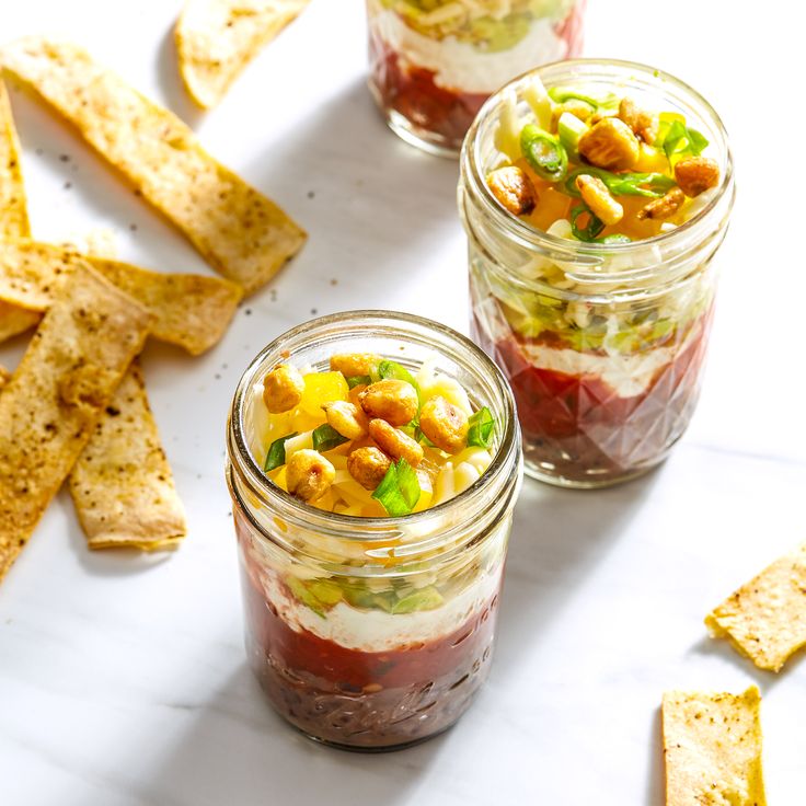 three small jars filled with food next to some crackers and chips on a table