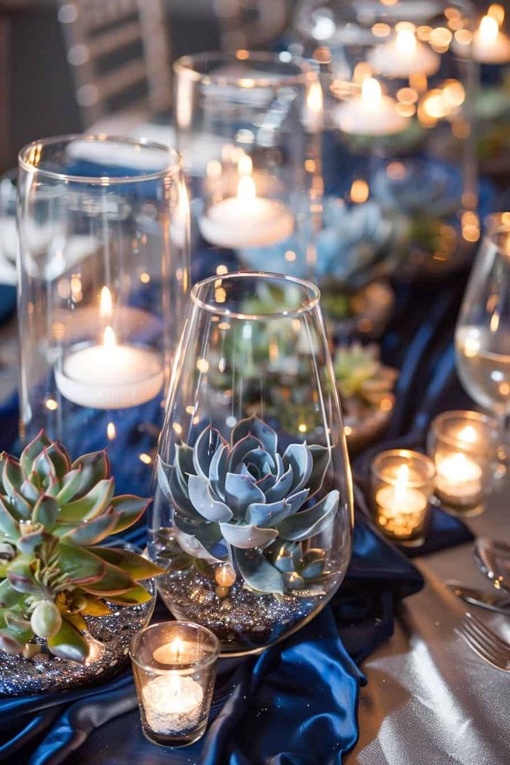 an arrangement of succulents and candles on a table with blue satin cloth