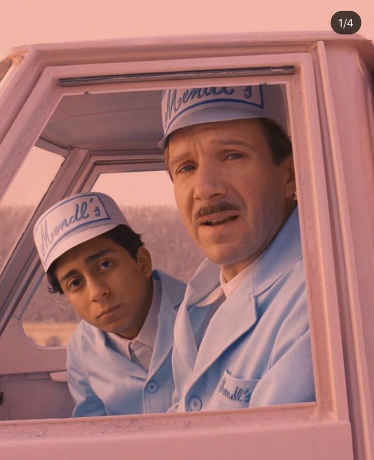 two men sitting in the driver's seat of a pink car looking at something