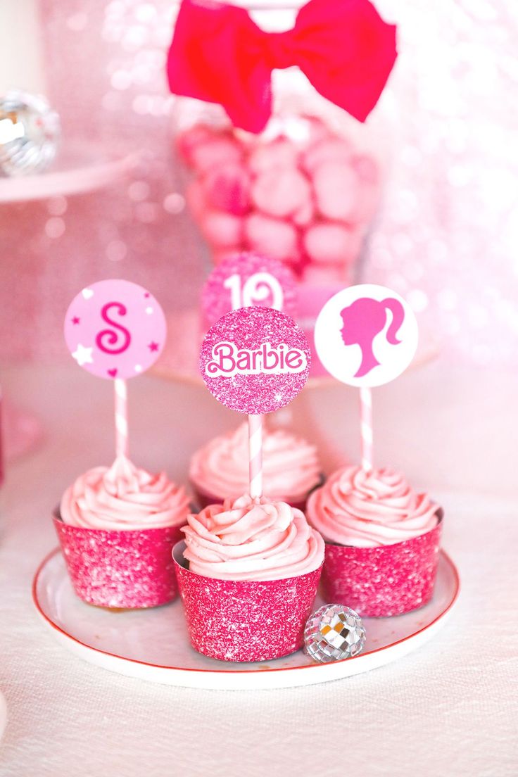 cupcakes with pink frosting and decorations are on a plate near other desserts