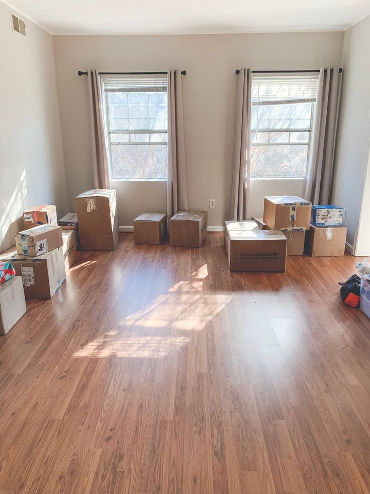 an empty room with boxes on the floor and two windows in the corner, all lined up