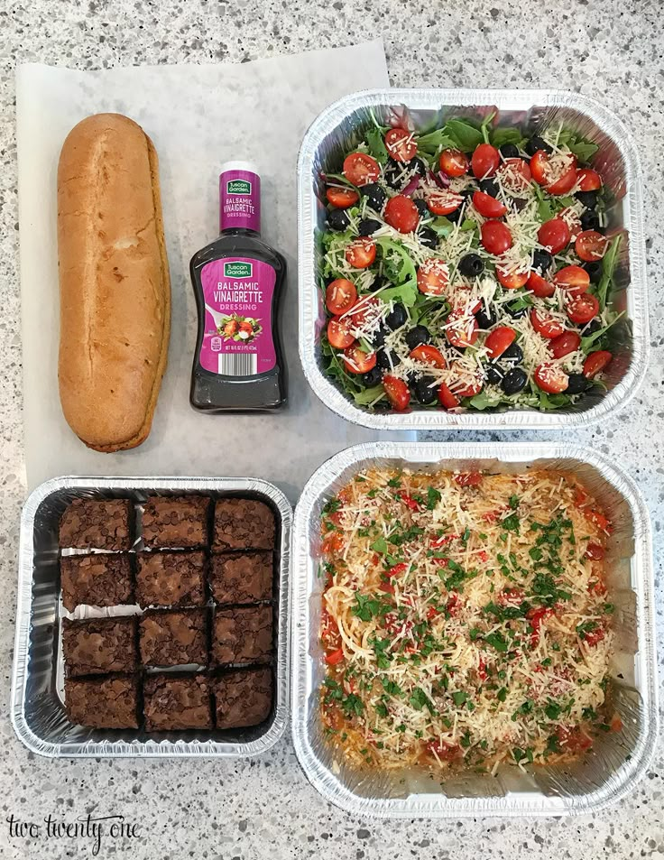 four plastic containers filled with food on top of a marble countertop next to a hot dog bun