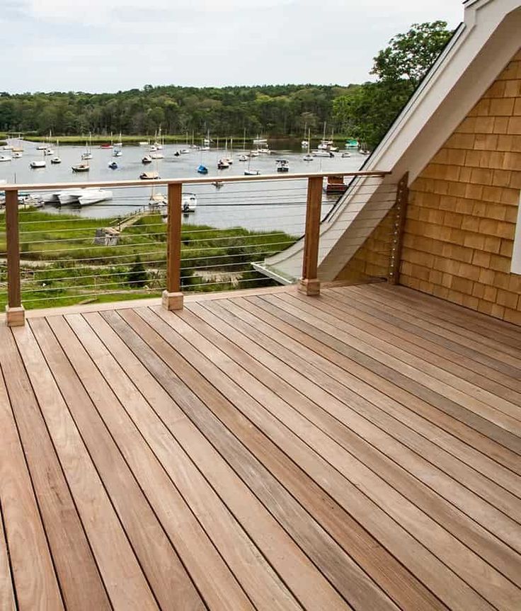 a wooden deck with boats on the water in the back ground and a house next to it