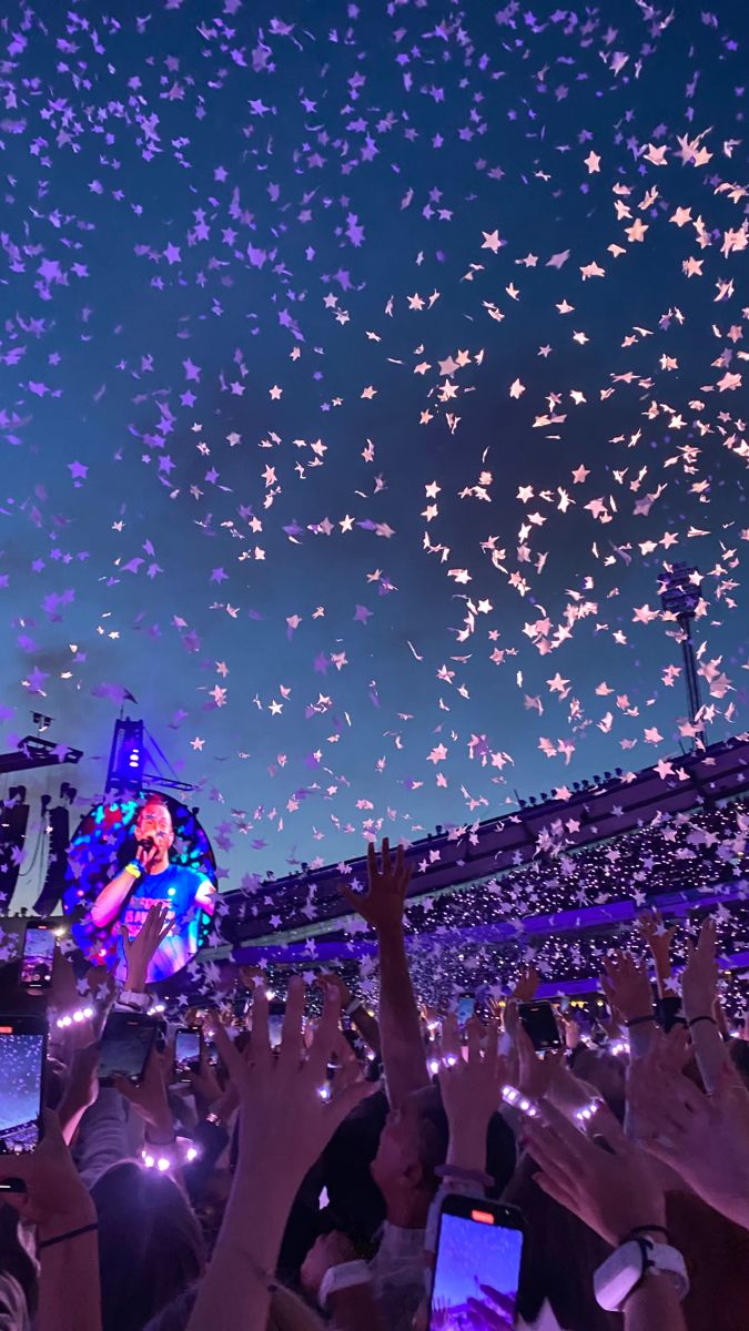 a crowd of people at a concert with their cell phones in the air and confetti falling from the sky