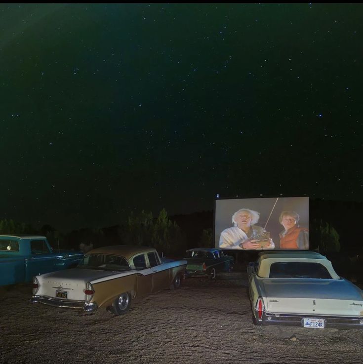 several cars parked in the dirt near a movie screen