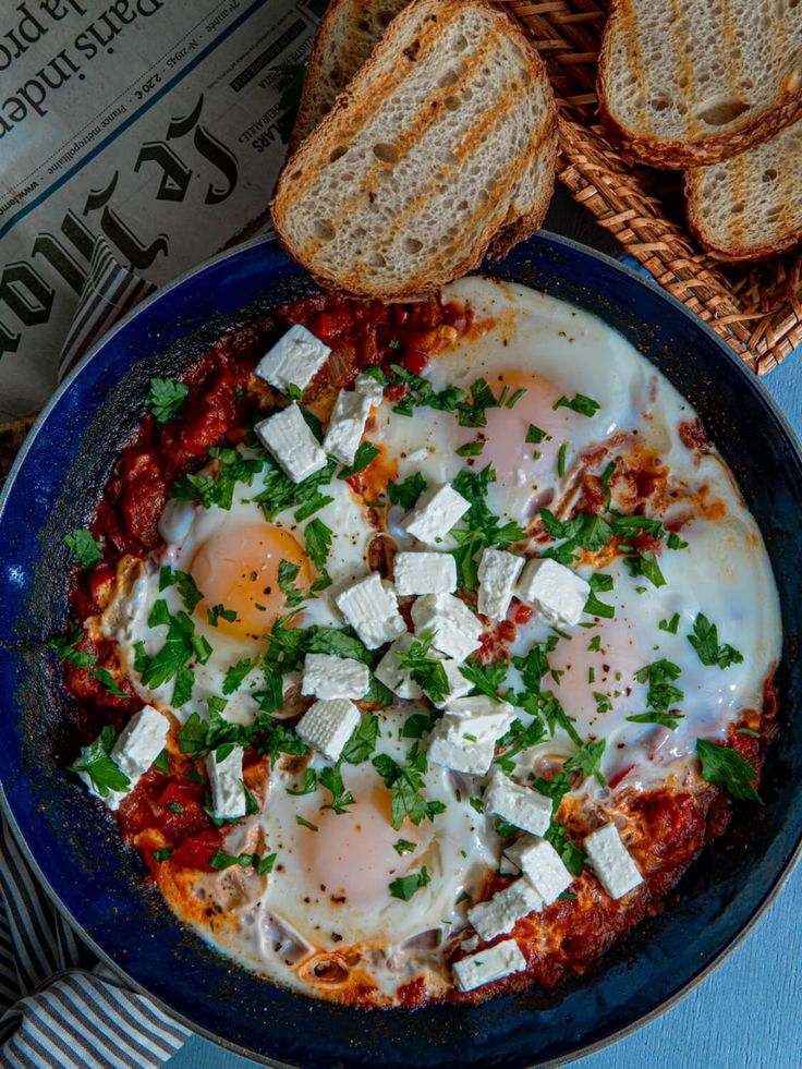 an egg and cheese dish in a blue bowl with bread on the side next to it