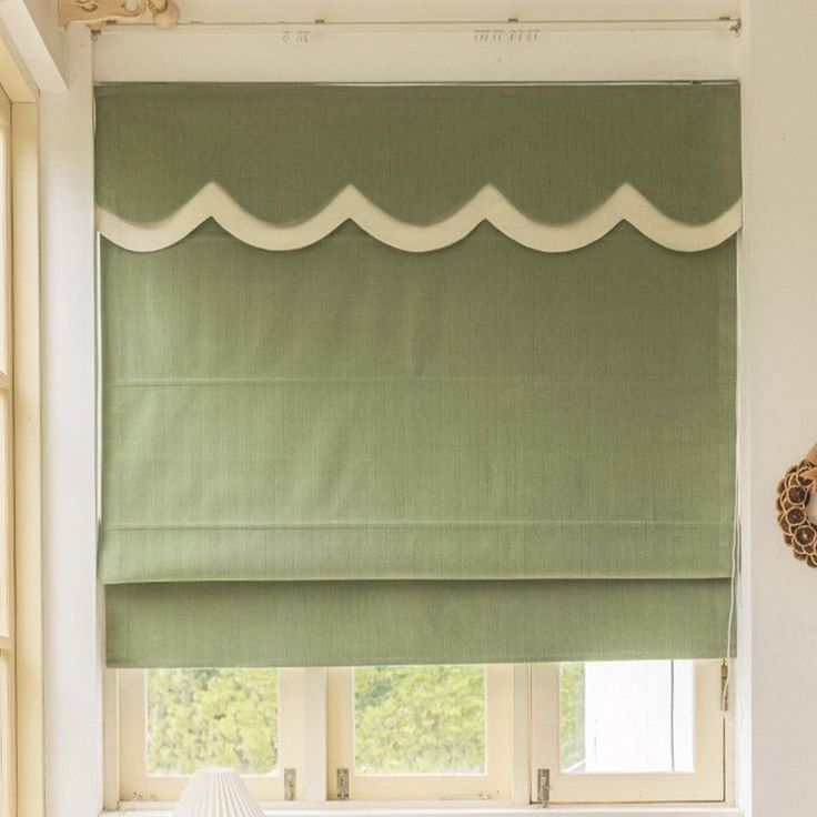 a green roman blind with white scallops on the top and bottom, in front of a window