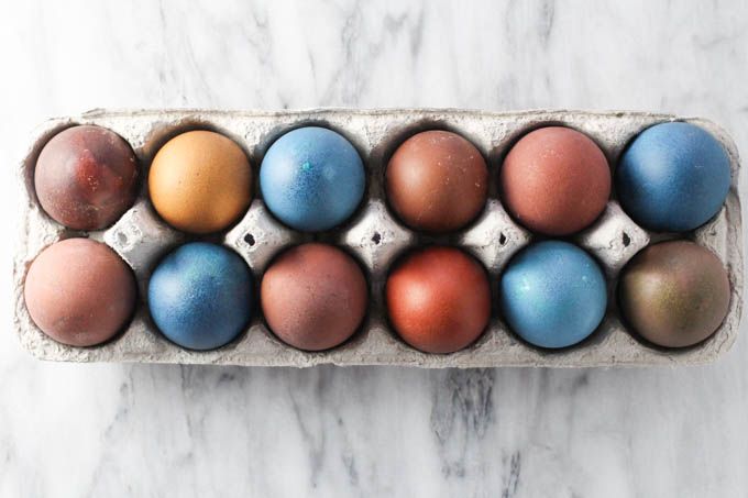 an egg carton filled with different colored eggs on a marble countertop, top view