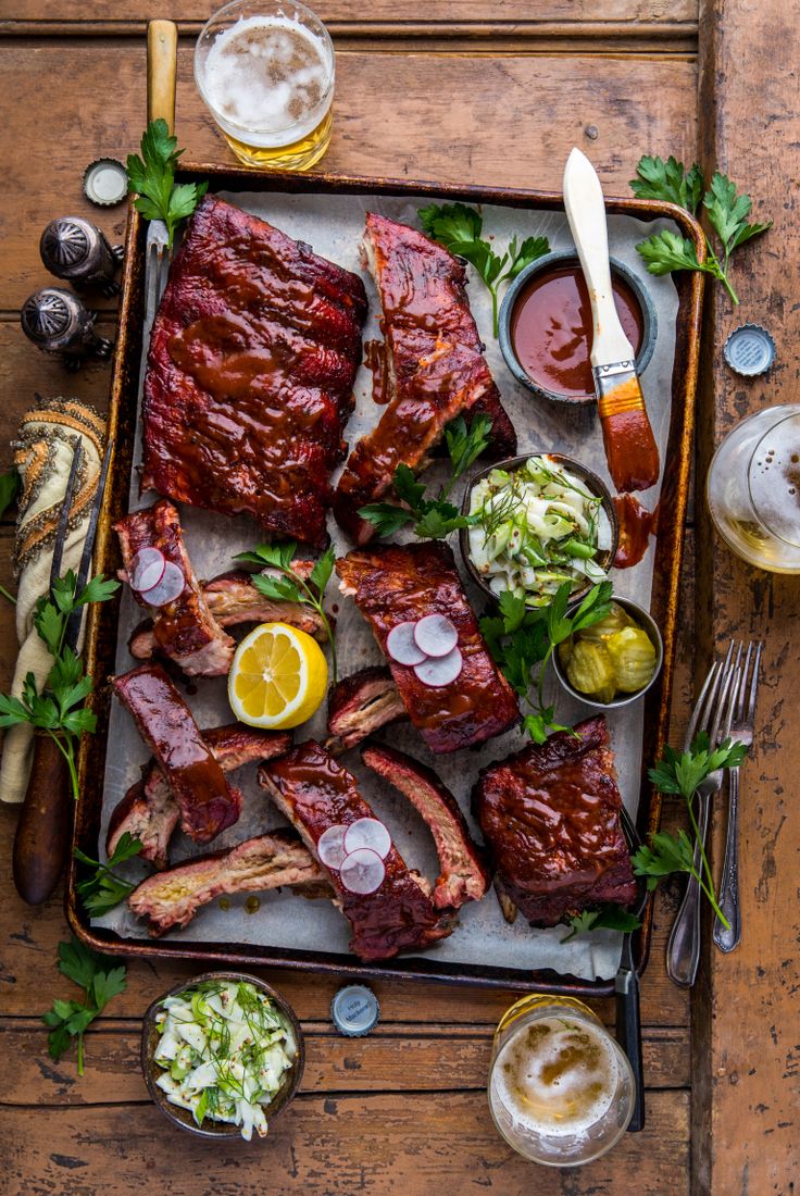 a tray with ribs, coleslaw and sauces on it next to other foods