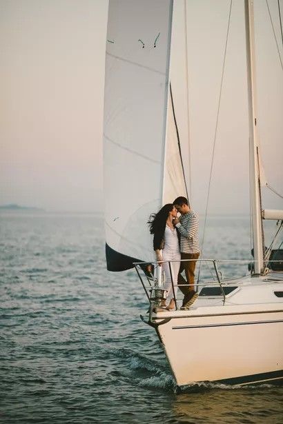 two people standing on top of a sailboat in the ocean