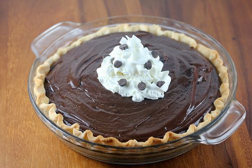 a chocolate pie topped with whipped cream and chocolate chips on a wooden table in a glass dish