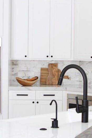 a kitchen with white cabinets and black faucet, marble counter tops and stainless steel appliances