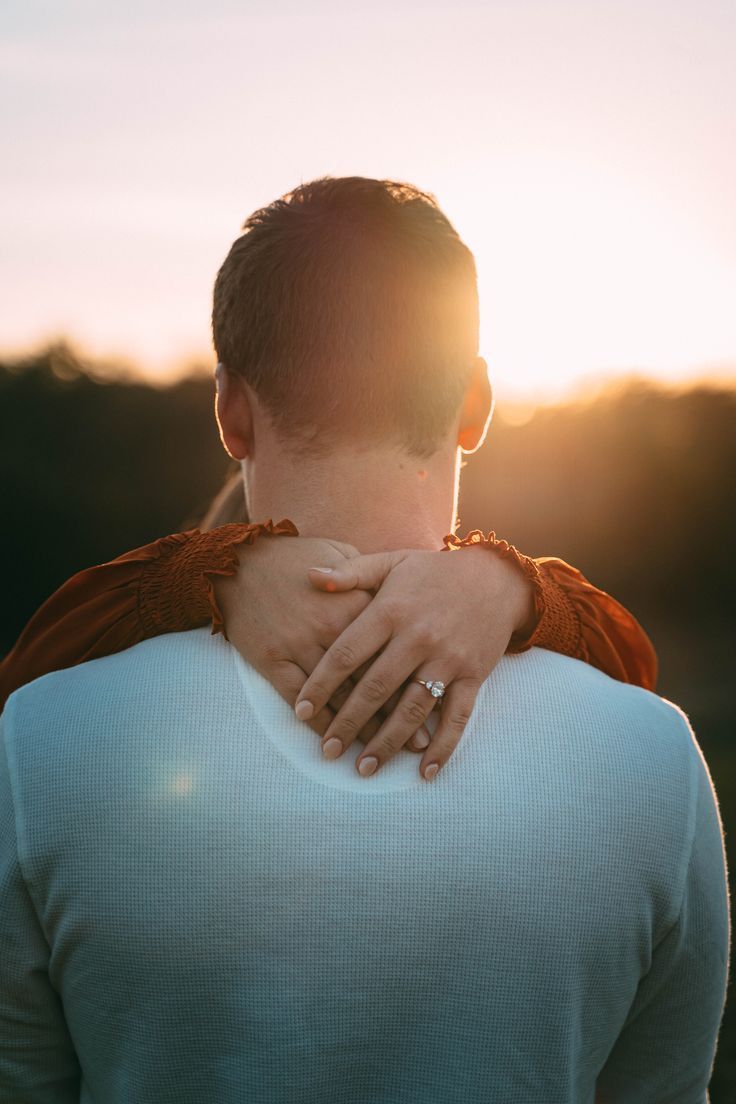 a man and woman embracing each other while the sun is setting