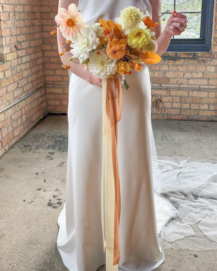 a woman in a white dress holding a bouquet of flowers and wearing an orange sash