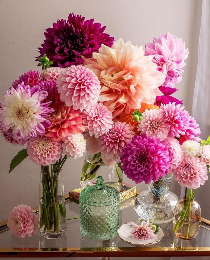 there are many different flowers in vases on the glass table and one is pink