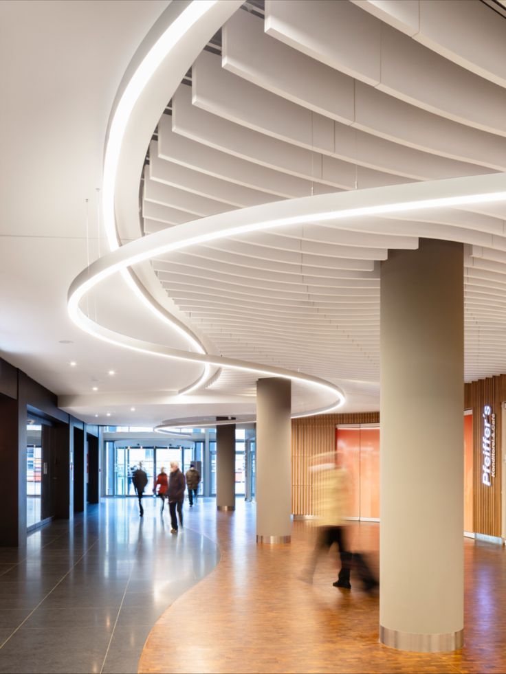 people are walking around in the lobby of an office building with circular lights and wood flooring