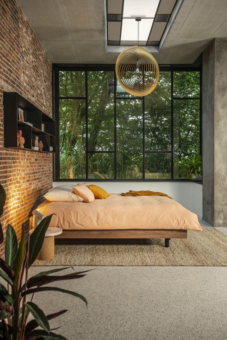 a bedroom with a brick wall and large windows in the ceiling, along with a bed that has yellow pillows on it