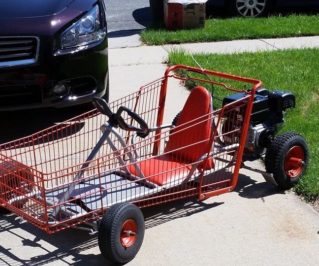 an orange shopping cart sitting on the sidewalk next to a black car and green grass