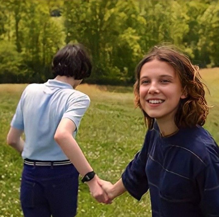 two people holding hands in a grassy field with trees in the background