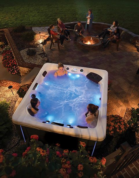 an outdoor hot tub lit up at night with people sitting in the back yard watching