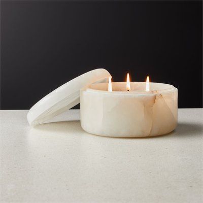 a white candle sitting on top of a counter next to a container with two candles in it