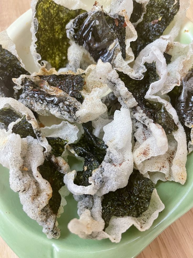 a green bowl filled with seaweed covered in powdered sugar on top of a wooden table