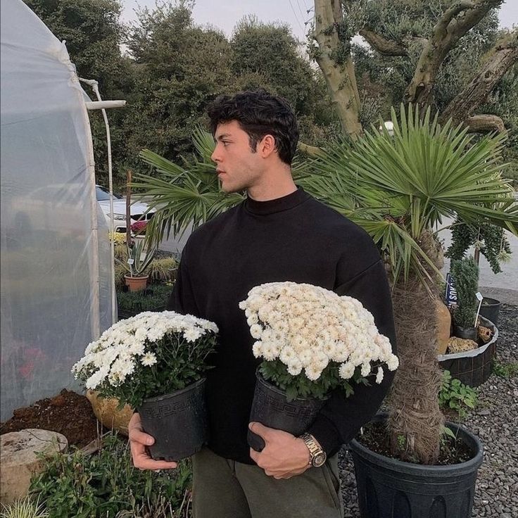 a man is holding two potted plants in front of a greenhouse with palm trees