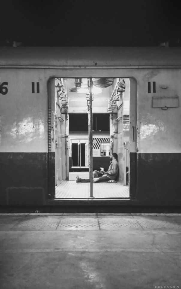 a black and white photo of a man sitting on a train door way with his feet in the open