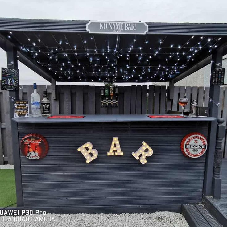 an outdoor bar with lights and decorations on the roof, in front of a fence