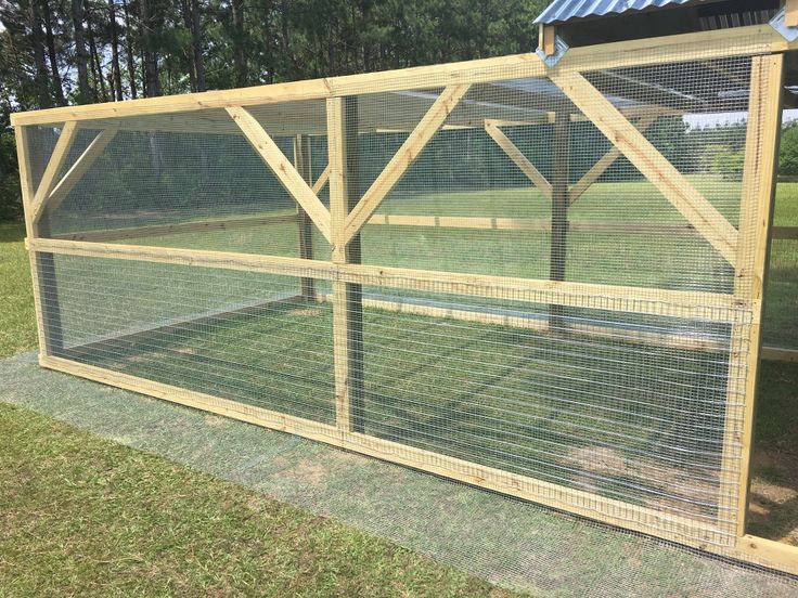 a large chicken coop in the middle of a field with grass and trees behind it