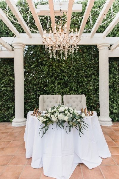 a table with white flowers and greenery on it in front of a chandelier