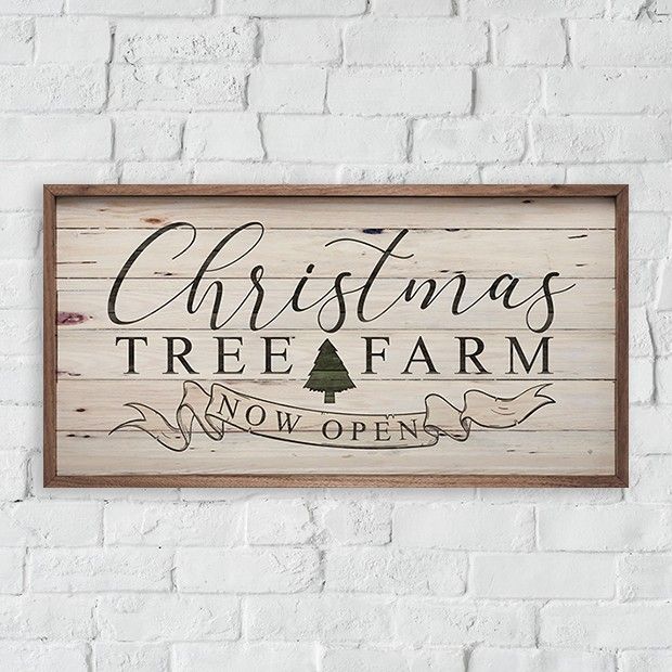 christmas tree farm sign mounted on a brick wall in front of a white brick wall