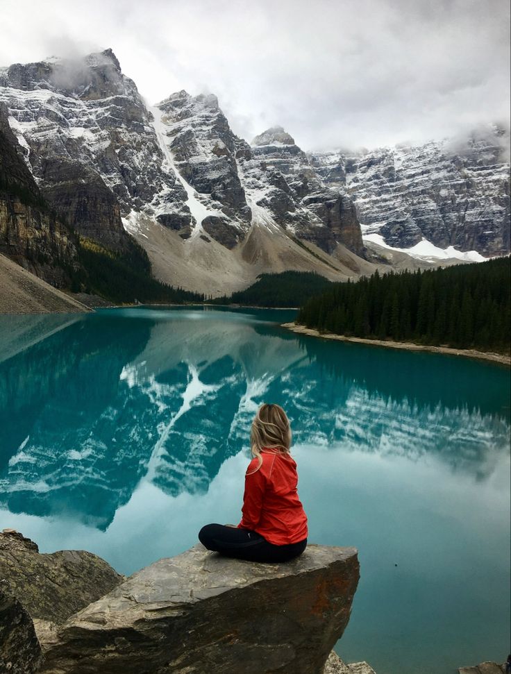 a woman sitting on top of a rock next to a lake filled with blue water